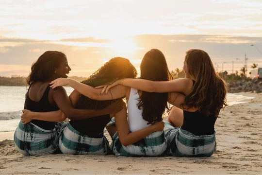 group of women sitting together arms around each other on beach