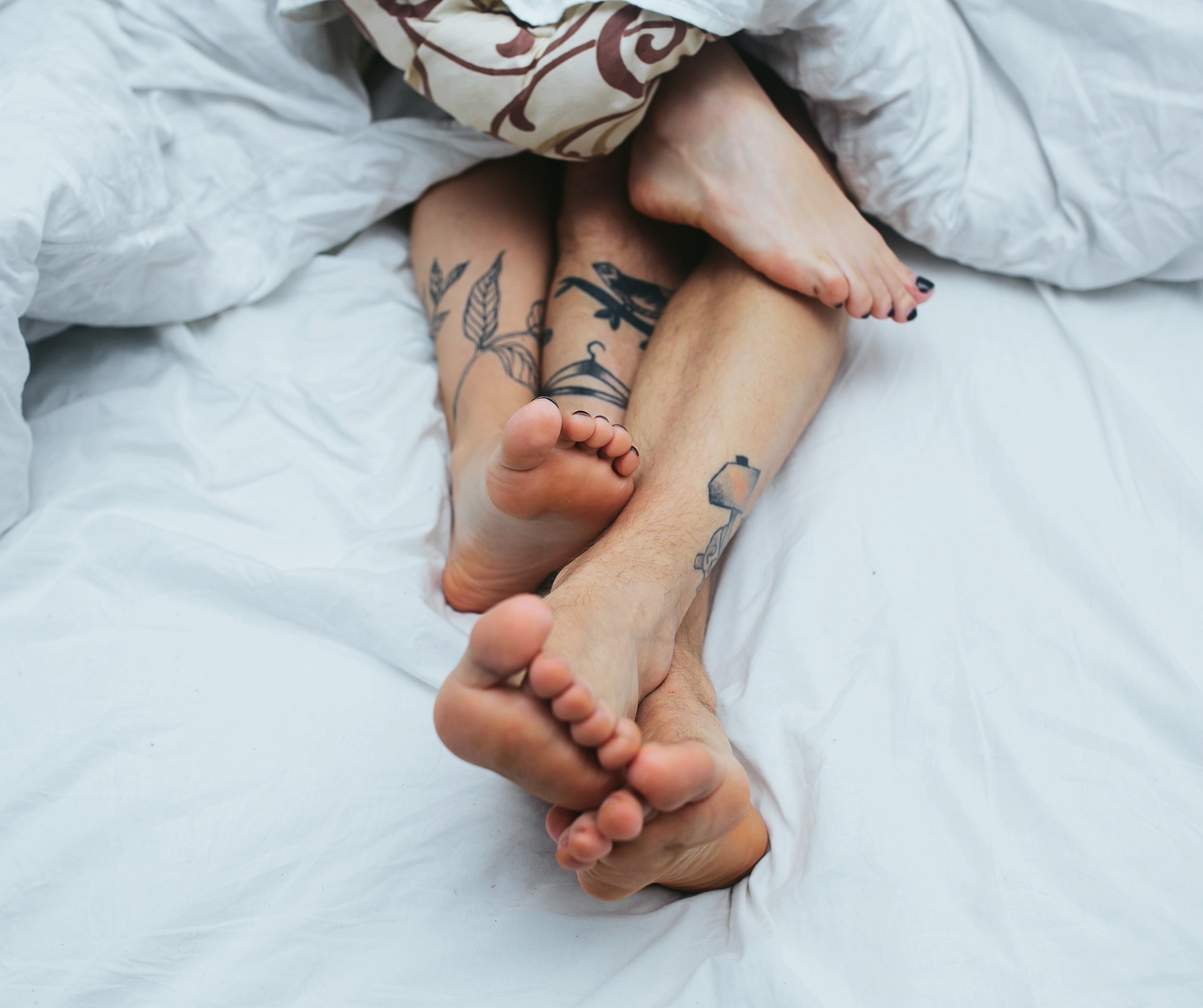 couple's feet hanging out of bed covers 